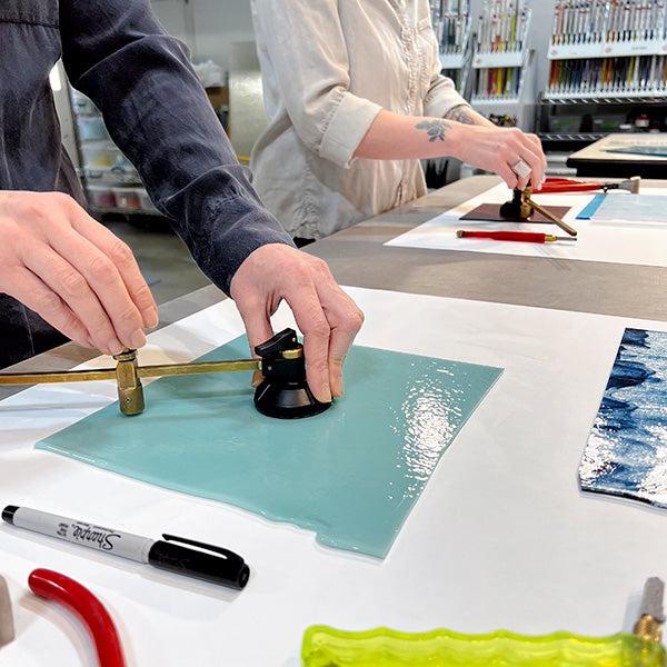 Two people are cutting circles out of glass